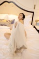 A woman sitting on a bed covered in a white sheet.