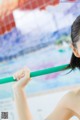 A woman holding a green pole in front of a swimming pool.