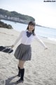 A woman in a school uniform is walking on the beach.