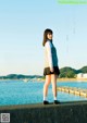 A young woman standing on a pier by the water.